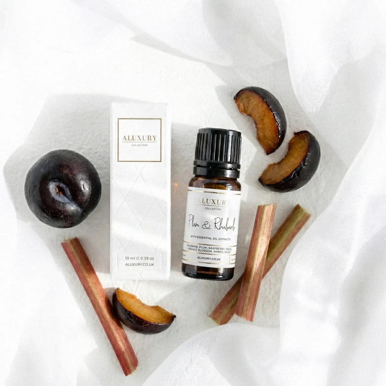 Bottle of Aluxury plum and rhubarb essential oil with plums and rubarb sticks on a white background