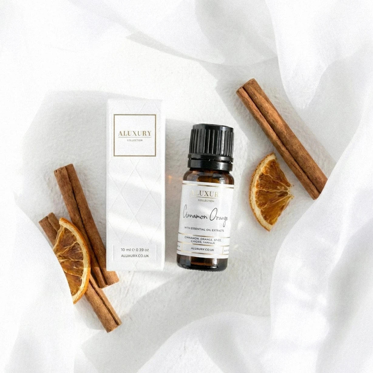 Bottle of cinnamon orange essential oil with packaging and cinnamon sticks on a white fabric background
