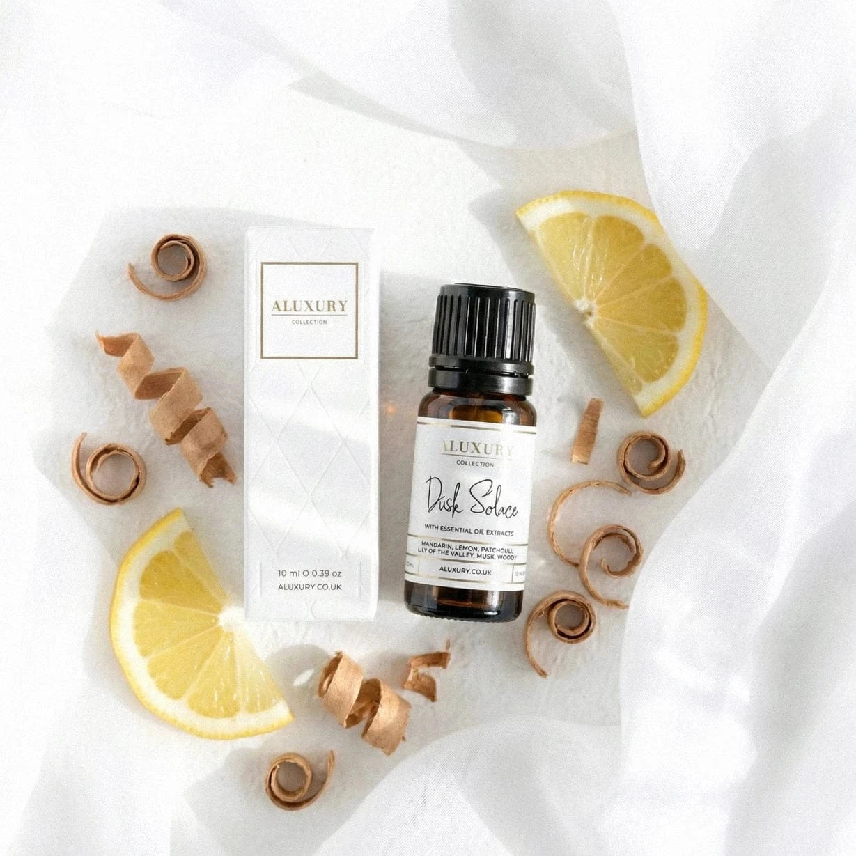 Aluxury dusk solace essential oil bottle with packaging on a white background with lemon slices and cinnamon sticks.