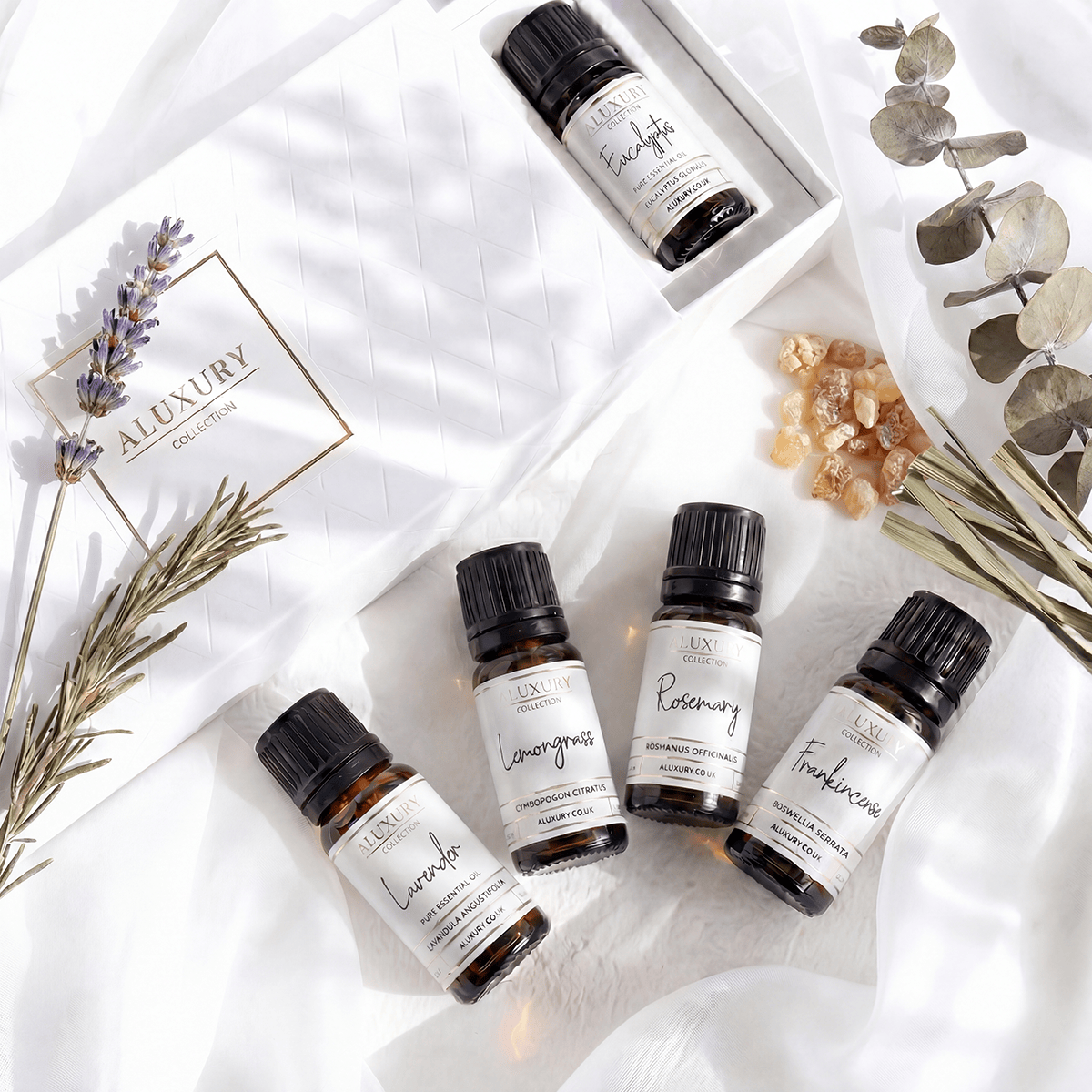 Collection of essential oil bottles with labels on a white surface with herbs and crystals.