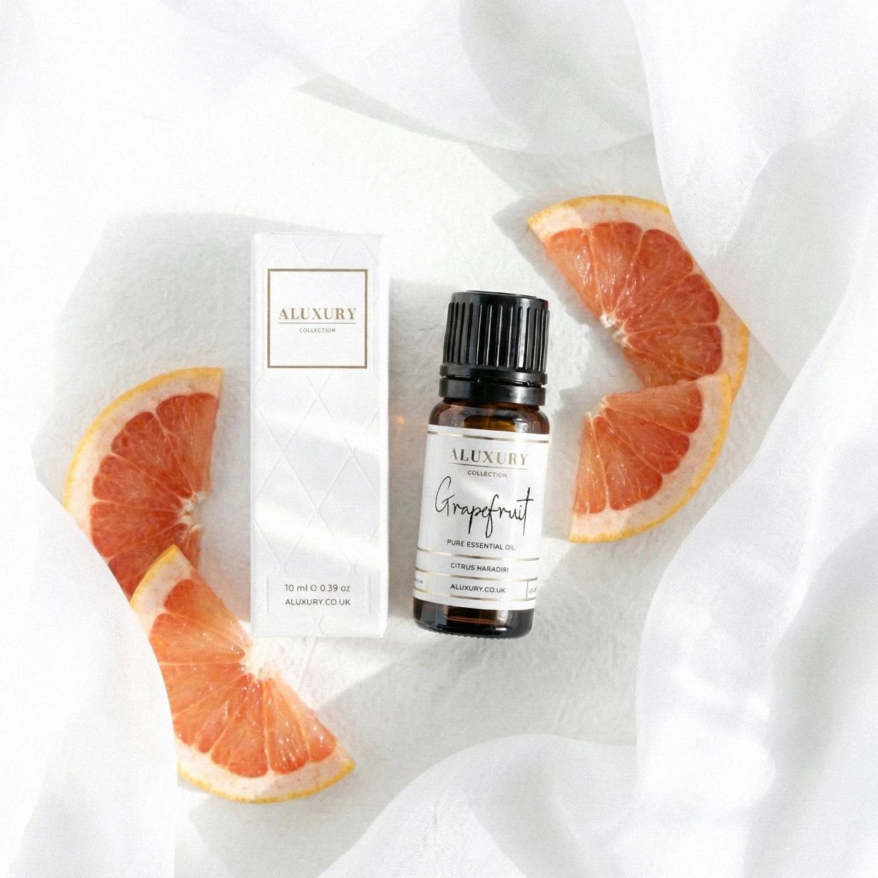 Aluxury grapefruit essential oil bottle and packaging on a white fabric background