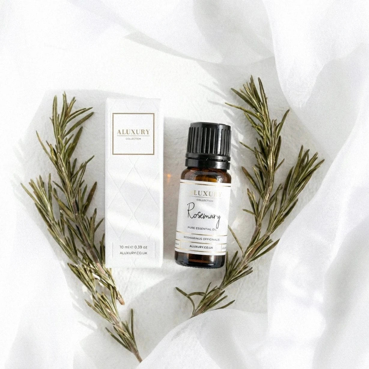 Bottle of Luxe Rosemary essential oil with packaging on a white fabric background