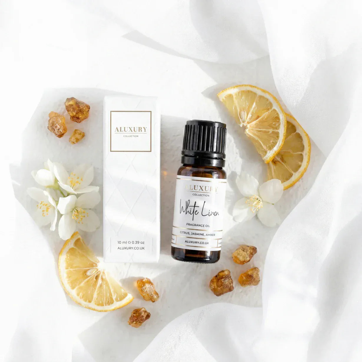 Aluxury brand essential oil bottle with packaging, lemon slices, and flowers on a white background