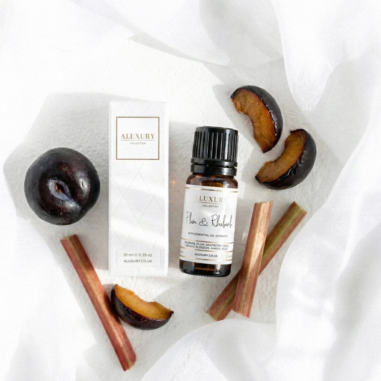 Bottle of Aluxury plum and rhubarb essential oil with plums and rubarb sticks on a white background