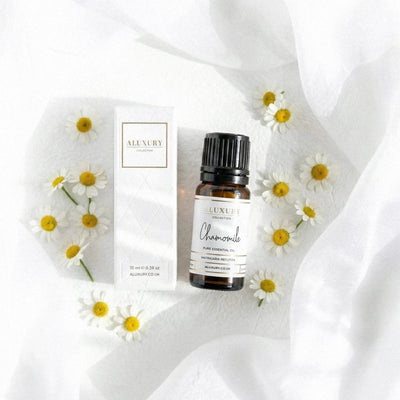 Aluxury chamomile essential oil bottle and packaging on a white fabric background with daisies.