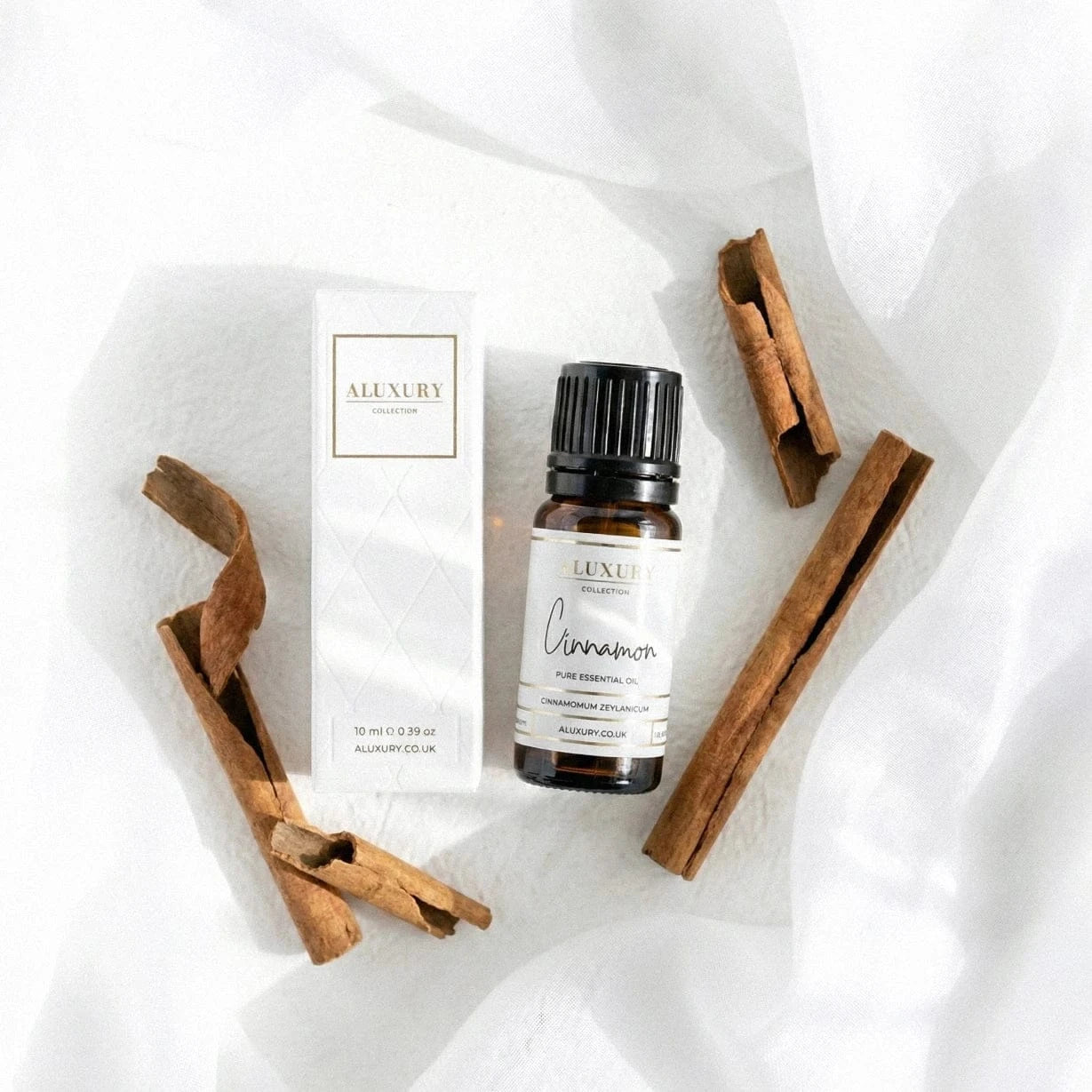 Aluxury cinnamon essential oil bottle with packaging and cinnamon sticks on a white fabric background