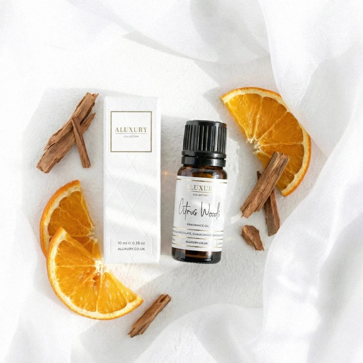 Bottle of Aluxury Citrus Woods fragrance oil with orange slices and cinnamon sticks on a white background