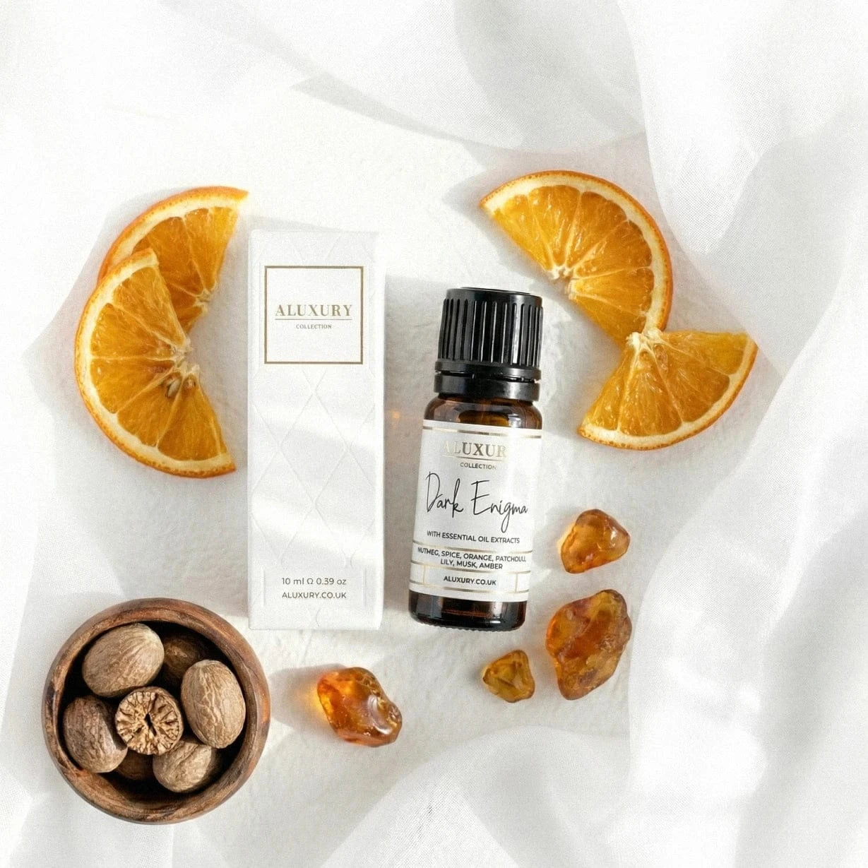Aluxury essential oil bottle with packaging, oranges, and nuts on a white fabric background