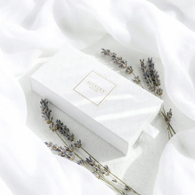 White essential oil gift box with lavender sprigs on a white fabric background