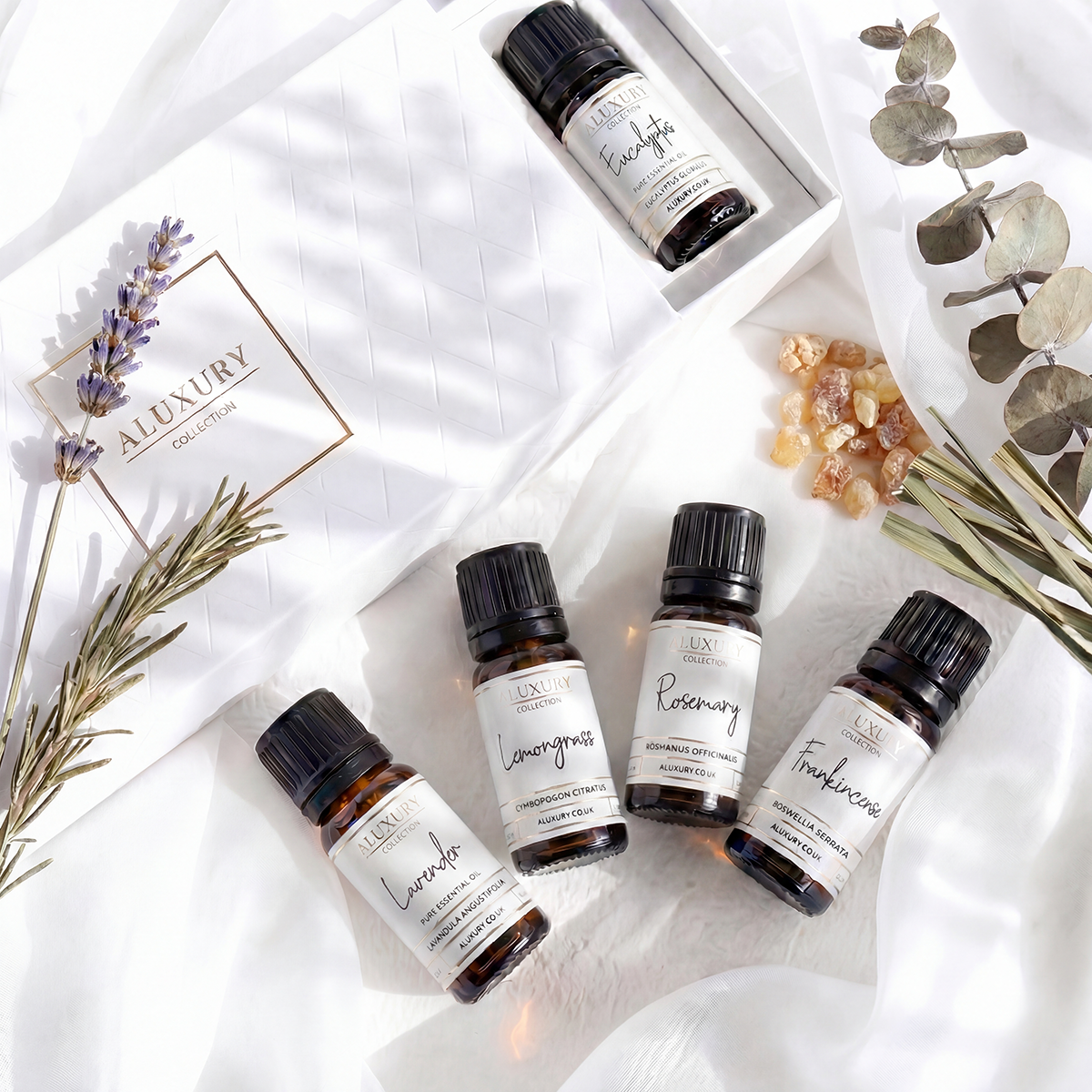 Collection of essential oil bottles with labels on a white surface with herbs and crystals.