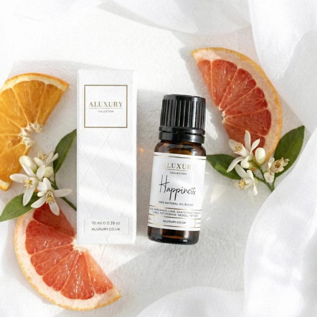 Aluxury Happiness essential oil blend bottle and packaging on a white fabric background