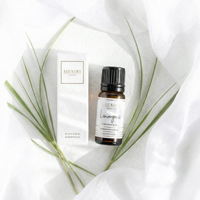 Luxury lemongrass essential oil bottle and packaging on a white fabric background with green leaves.