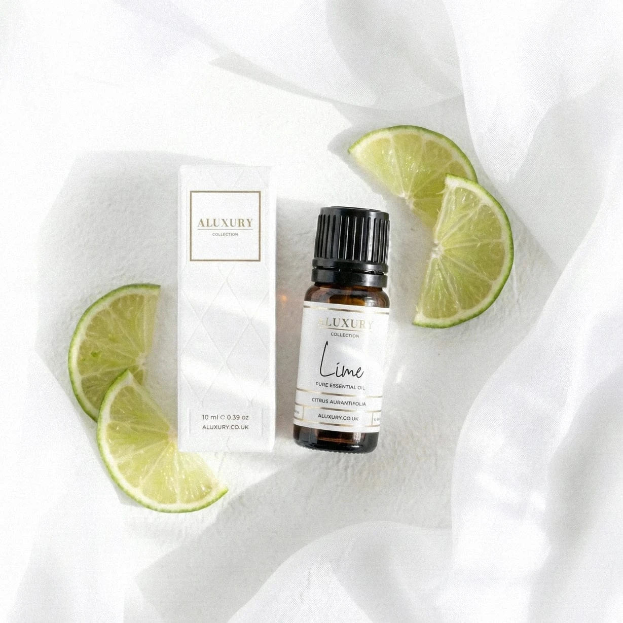 Aluxury Lime essential oil bottle with packaging and lime slices on a white fabric background