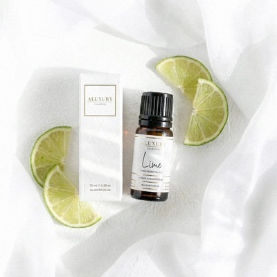 Aluxury Lime essential oil bottle with packaging and lime slices on a white fabric background