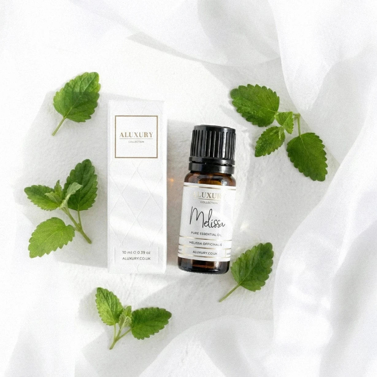 Bottle of Melissa essential oil with packaging and mint leaves on a white fabric background