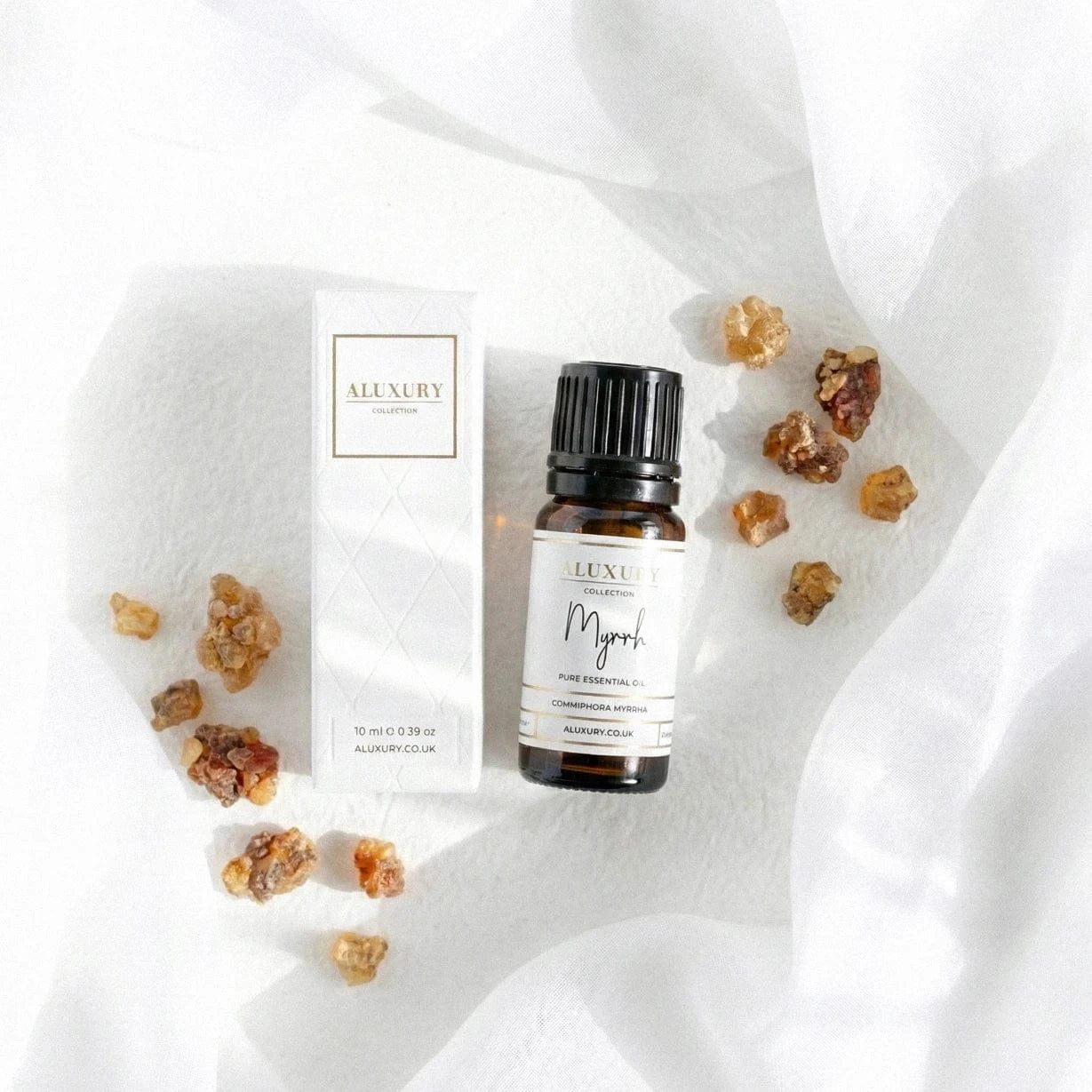 Aluxury essential oil bottle with packaging and myrrh resin on a white fabric background