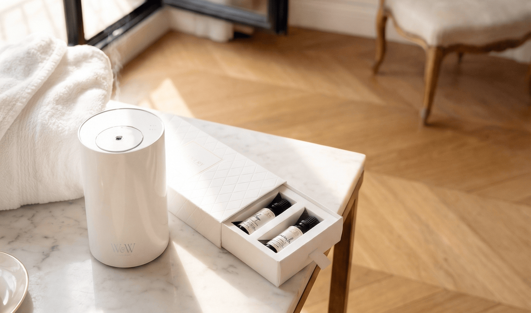 White Nebula diffuser with essential oils on a marble surface with a wooden floor in the background