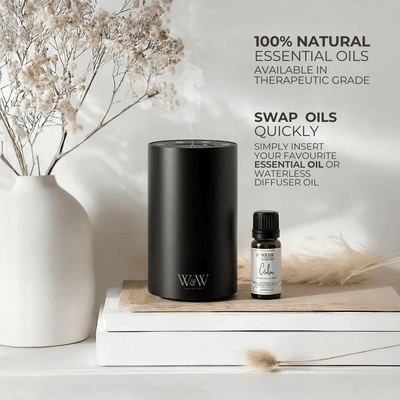 Black waterless diffuser and essential oil bottle on a wooden surface with decorative elements. 