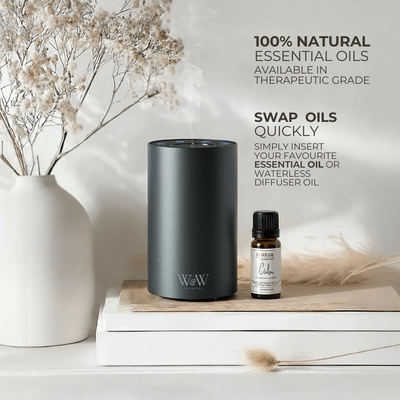 Grey waterless diffuser and essential oil bottle on a wooden surface with decorative elements. 