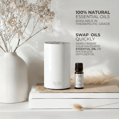 White waterless diffuser and essential oil bottle on a wooden surface with decorative elements. 