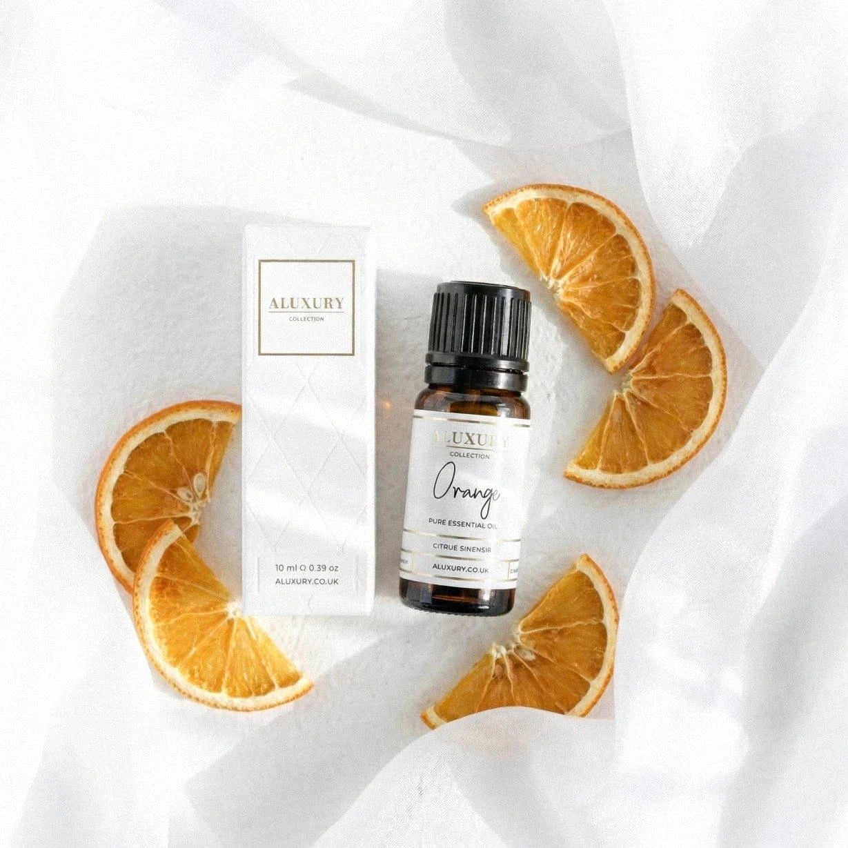 Aluxury orange essential oil bottle with packaging and orange slices on a white fabric background