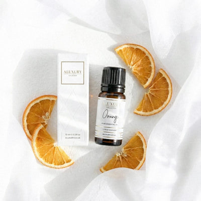 Aluxury orange essential oil bottle with packaging and orange slices on a white fabric background