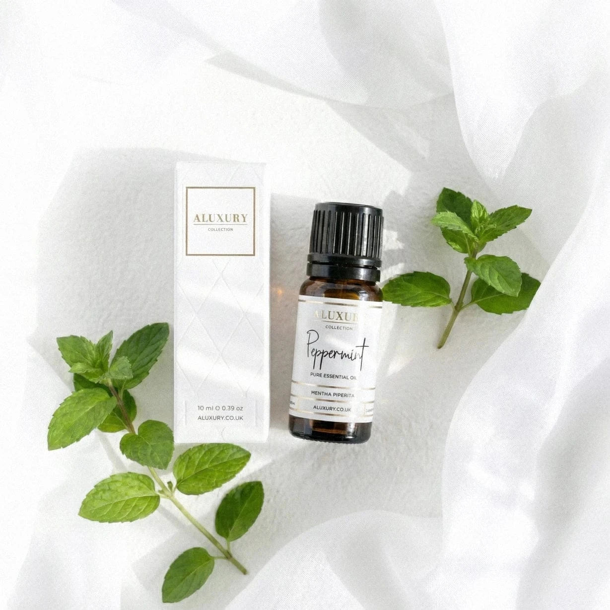 Aluxury peppermint essential oil bottle and packaging on a white fabric background