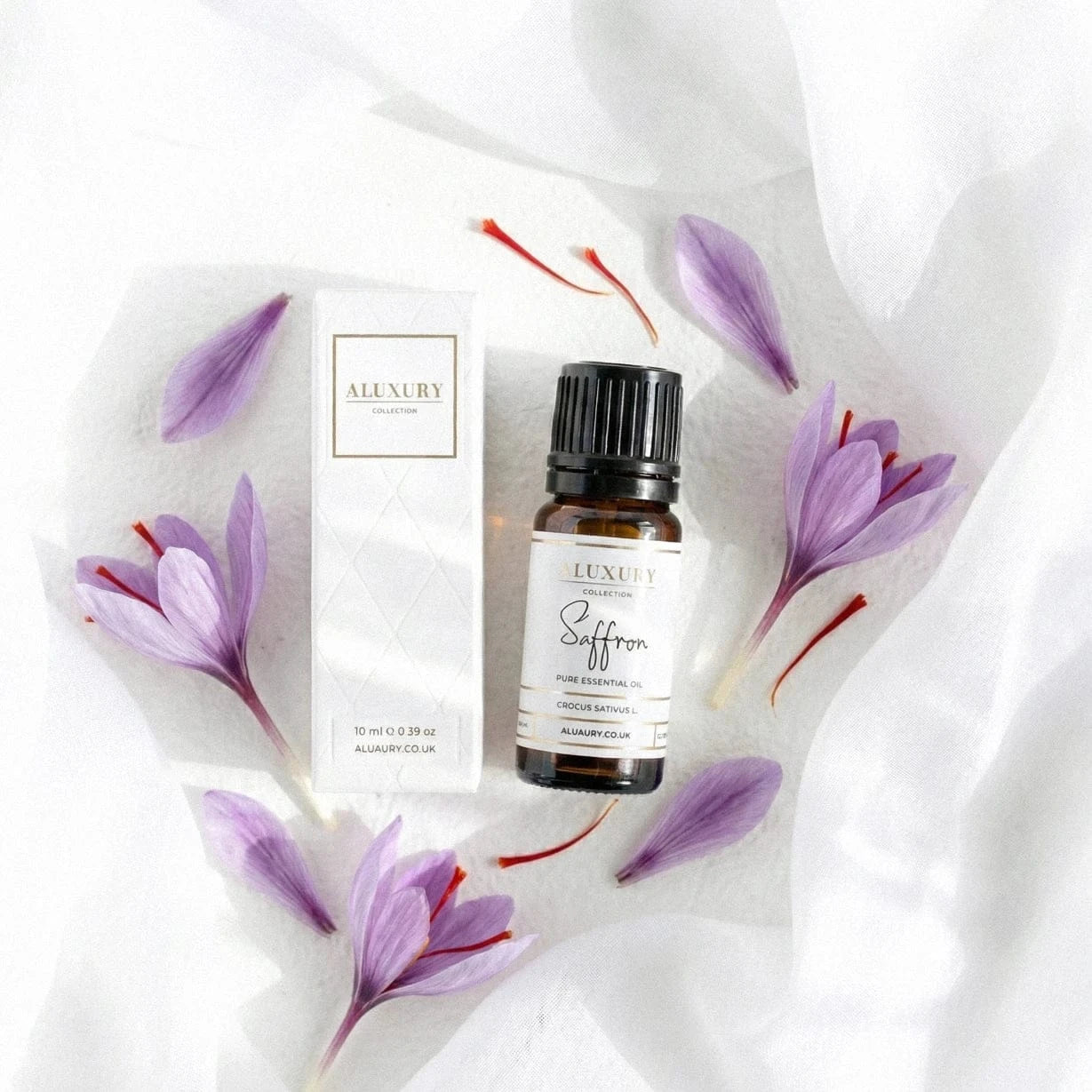 Saffron Essential Oil bottle with box and petals on a white textured background with fabric