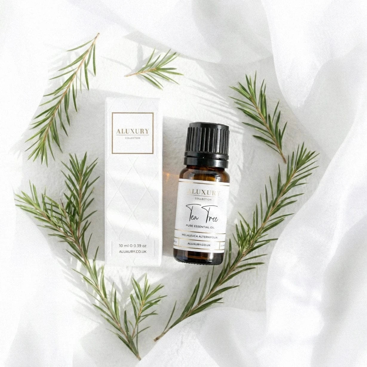 Luxury tea tree essential oil bottle with box and green leaves on a textured white background