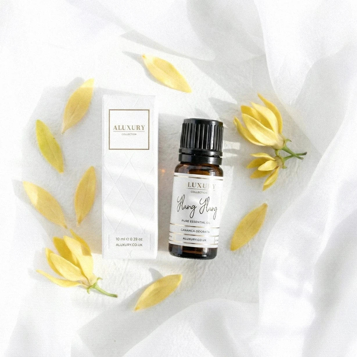 Luxury ylang ylang essential oil bottle and packaging with yellow flowers on a white fabric background